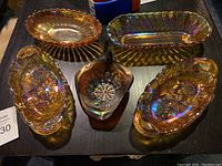 Five carnival glass bowls arranged on a table: four amber oblong shaped and one small blue bowl in the center.