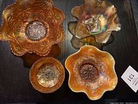 Four amber carnival glass bowls of different sizes and patterns arranged on a surface, showing the overall lot.