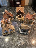 Six miniature collectible houses arranged on a granite countertop, showing a mix of tiled and thatched roofs with chimney details.
