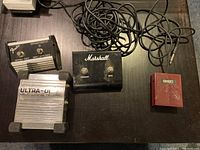 Top-down view of all four items showing Fender footswitch, Marshall footswitch box, Dixon pedal switch, and Behringer Ultra-DI box with cables.