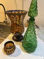 Photo showing the 12-candle holder, small pot candle holder, and vintage green bubble glass decanter together on a kitchen counter.