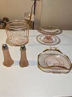 Full set of five pink depression glass items shown on table including cookie jar, candy bowl, napkin holder, salt and pepper shakers