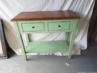 Full frontal view of distressed wooden table with two drawers and lower shelf, showing overall wear and paint distress.