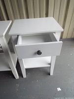 Photo of one white wooden end table with drawer open, showing drawer knob and bottom shelf.