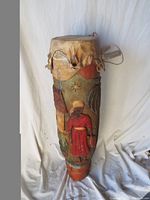 Full view of tall carved wood drum with painted and carved human figure.