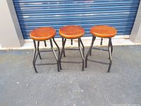 Front view of three adjustable stools with round wood seats and black metal legs.