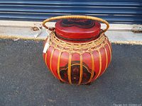 Side view of the round red painted basket with vertical bamboo strips and carved lid with handle