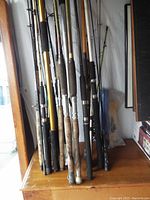 Fishing poles standing upright on a wooden surface, various handles visible, some showing wear and damage.