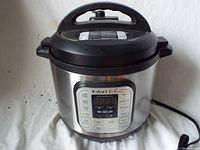 Front view of the Instant Pot IP-DUO showing the full appliance and lid closed. Stainless steel body with black top and base.
