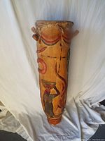 Full length view of the carved wooden drum showing colorful painted design and top rim damage.