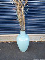 Full view of the large light blue Jenkins vase with some decorative sticks inside. Shows the vase's general shape and color.