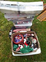 Box with assorted Christmas decorations including stockings, ornaments, tin container, wrapping paper, and ribbons.