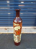 Front view of tall brown metal vase with embossed floral design