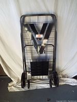 Full view of black metal frame folding cart standing upright with large wheels and wire basket.
