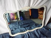 Full view of the scalloped edge oval mirror standing against a backdrop, showing the shape, frame detailing, and condition.