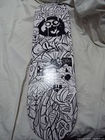 Front of skateboard deck showing detailed black and white graffiti-style artwork with cartoon faces and abstract shapes.