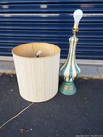 Full view of teal harlequin ceramic lamp and striped fabric shade placed on ground with cord and bulb installed