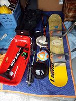 Full lot showing a red sled with handles, snowboard, hockey sticks, baseball bats, golf bag, and balls