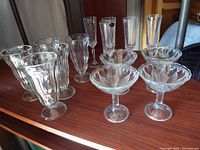 Wide view of all glass stemware displaying dessert bowls and assorted tall glasses on wood surface