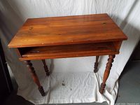 Full view of vintage wooden desk showing top surface, turned legs, partial slide-out board.