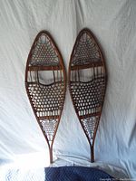 Full view of the pair of vintage Tubbs snowshoes showing wooden frames and rawhide webbing.