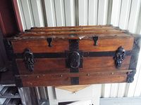 Front view of vintage wooden chest showcasing metal straps, black metal latches, and central lock plate