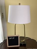 Front view of lamp with white drum shade, brass U-shaped stem, and marble base on wooden table.