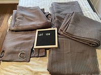 Set of four folded brown curtain panels laid on a bed, showing metal eyelets and overall fabric pattern.