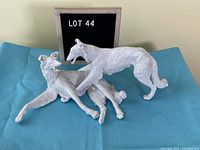 Photo showing white porcelain dog sculptures with textured fur arranged on blue surface with lot 44 sign
