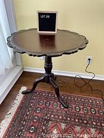 Front angle view of the vintage round fold top occasional table showing carved edge and three legs on a patterned rug.