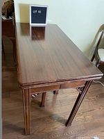 Side view of the folded dining table showing the wooden legs with decorative carved supports and polished finish.