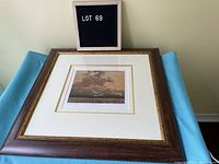 Framed Tom Thomson print titled "Thunderhead" resting on light blue fabric with a LOT 69 sign next to it.