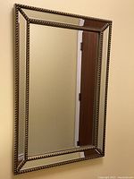 Full view of the rectangular mirror showing the gold upholstery tack design frame and angled outward edges.
