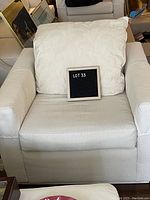 Front view of oversized white upholstered club chair with wide base, set on wood floor, shows the chair with large white floral pattern cushion on seat back.