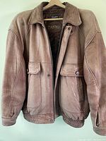 Front view of the men's tan leather jacket showing overall color, structure, elastic waistband, and flap pockets.