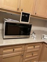 Microwave oven on a kitchen countertop with cabinets above. Panasonic branding visible on the oven front.