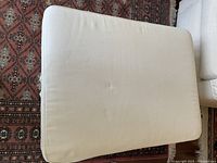 Top view of the white upholstered storage ottoman, showing the removable cushioned top with slight fabric wrinkles and minor marks visible.