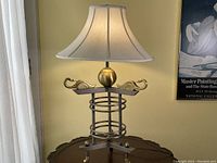 Full view of metal table lamp showing white bell shade, spiral base, and two brass swan figures.