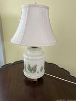 Full view of the ceramic lamp showing the white bell-shaped shade, painted fern design on ceramic base and unusual finial on top.