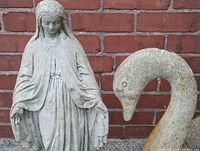 Close-up of the religious figure statue showing detailed facial features, robes, and hands with a cement weathered texture.
