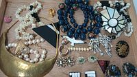 Photo of assorted costume jewelry on wooden tray showing variety of necklaces, brooches, earrings, and rings.