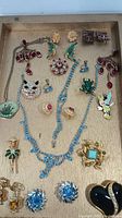 Photo showing all jewelry pieces displayed on wooden tray, clear view of earrings, necklaces, brooches, and pins included in lot