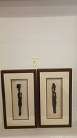 Two framed wooden female sculptures of African origin, displayed side by side against a white wall