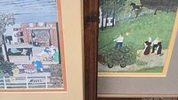 Close-up of two stacked framed Grandma Moses folk art prints showing signature and part of images