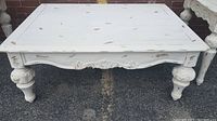 Front view of a white hand painted wooden coffee table with carved apron and rounded sculpted legs.