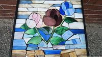 Close-up of the mosaic glass top showing the flower pattern in pink, brown, blue with green leaves and blue/white/beige background pieces