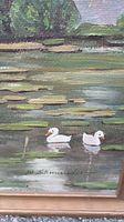 Close-up of painting detail showing signature and two white ducks swimming among lily pads.