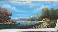 Frontal view of oil on canvas painting showing scenic landscape with lake, cabin, sailboat, trees, and mountains under blue sky with clouds.