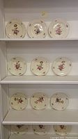 Set of 9 ivory tone floral soup plates with gold rim arranged on white shelves