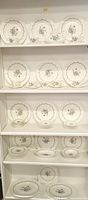 Shelf displaying multiple plates, bowls, and cups with Chelsea Rose floral design and scalloped edges